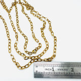 golden oval cable chain necklace with lobster claw clasp above stainless steel imperial ruler on white background. 