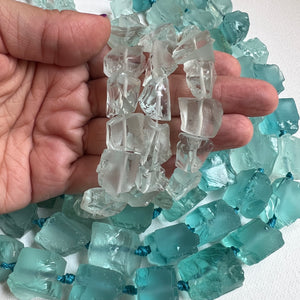 small pale blue and larger blue-green rough cut fluorite nuggets on a white background