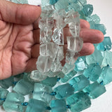 small pale blue fluorite rough cut nuggets in a hand to show scale with darker blue green fluorite nuggets in the background