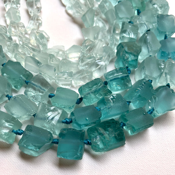 small pale blue and larger blue-green rough cut fluorite nuggets on a white background