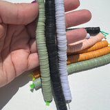 sage green, black, and blue grey African vinyl disk beads held in a hand to show scale on a white background