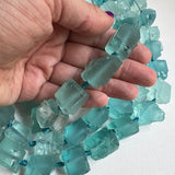 blue green transparent rough cut nuggets in a hand to show scale on a white background