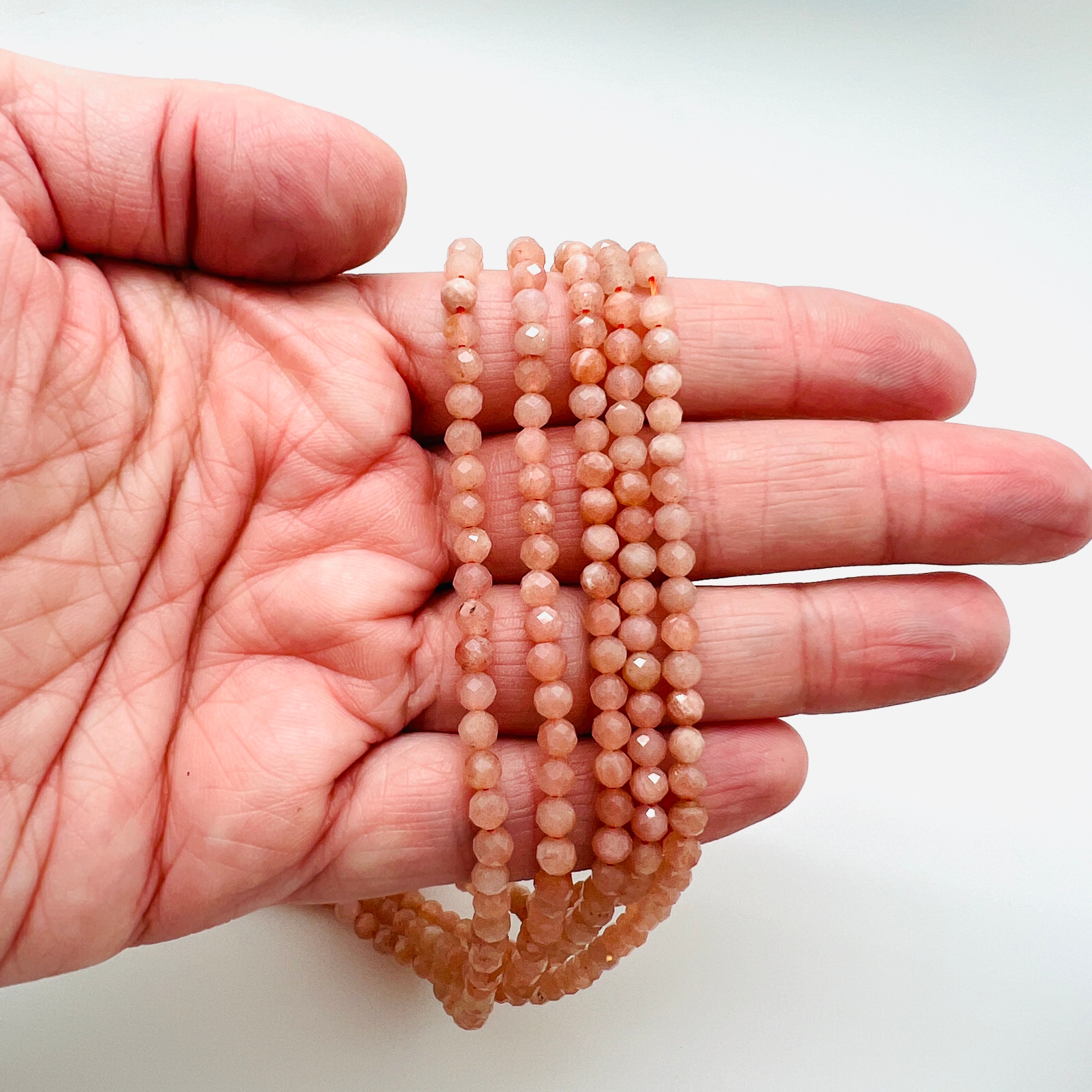 five faceted round sunstone bead strands draped over a hand with white background.