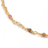zoomed in section of golden chain and multi-colored tourmaline faceted round beaded necklac over white background. 
