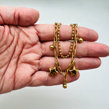 golden double layered, paperclip and ball chain bracelet displayed on a hand with  white background.  the paperclip chain dangles alternating ball and star charms. 