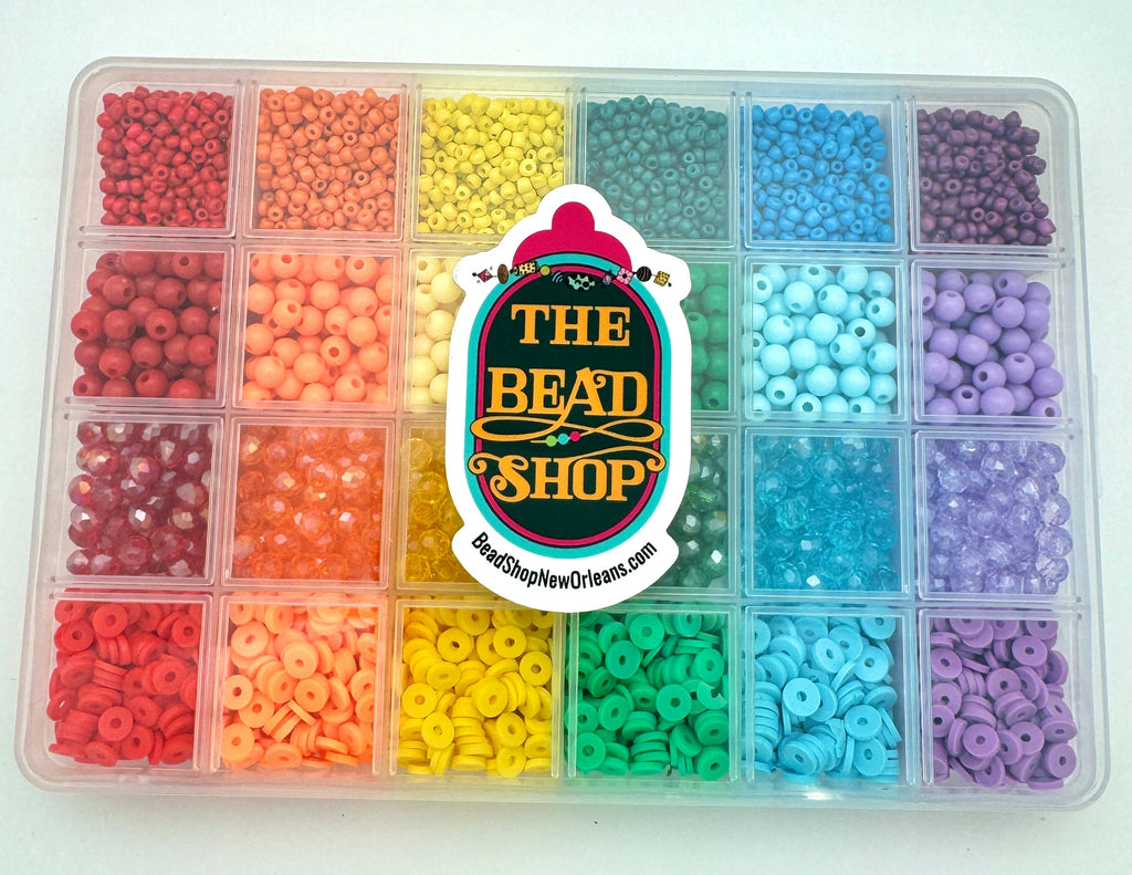 twenty-four compartment plastic storage bead box filled with four different styles of the six different rainbow colors of beads over white background with "The Bead Shop" logo on the front. 