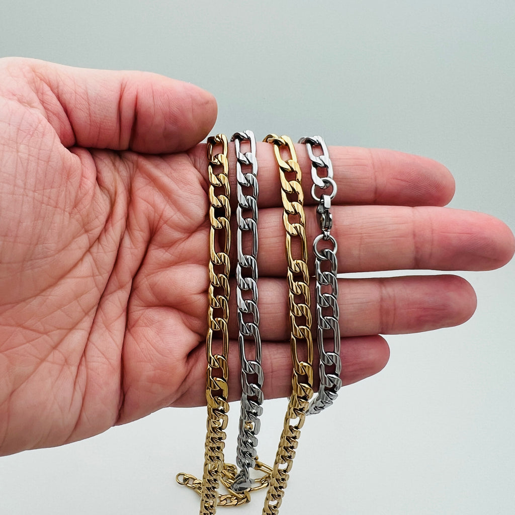 two silver tone and two golden textured Figaro link chains draped over a hand on a white background.