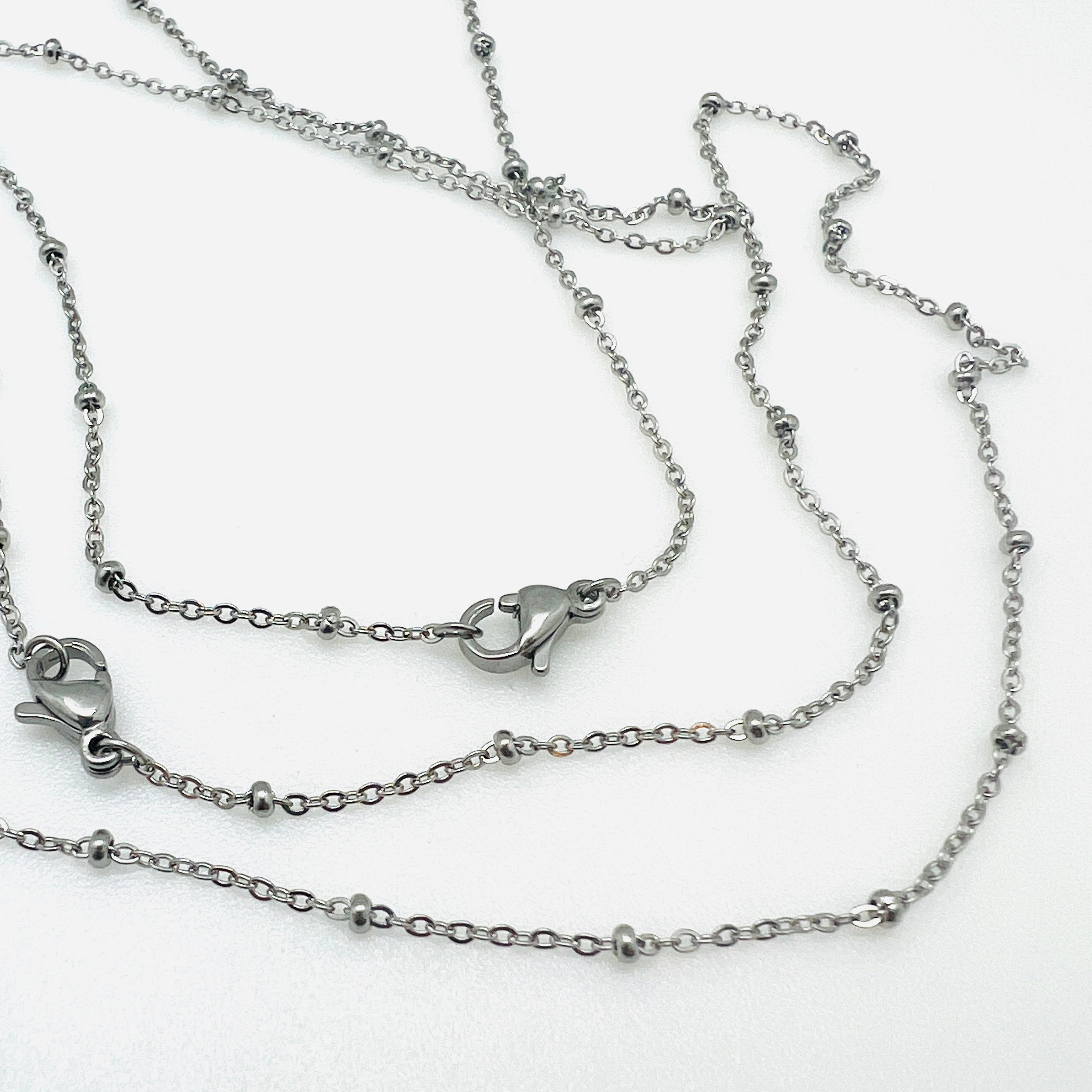 silver tone satellite chain necklace with rondelle beads and lobster claw clasp over white background. 
