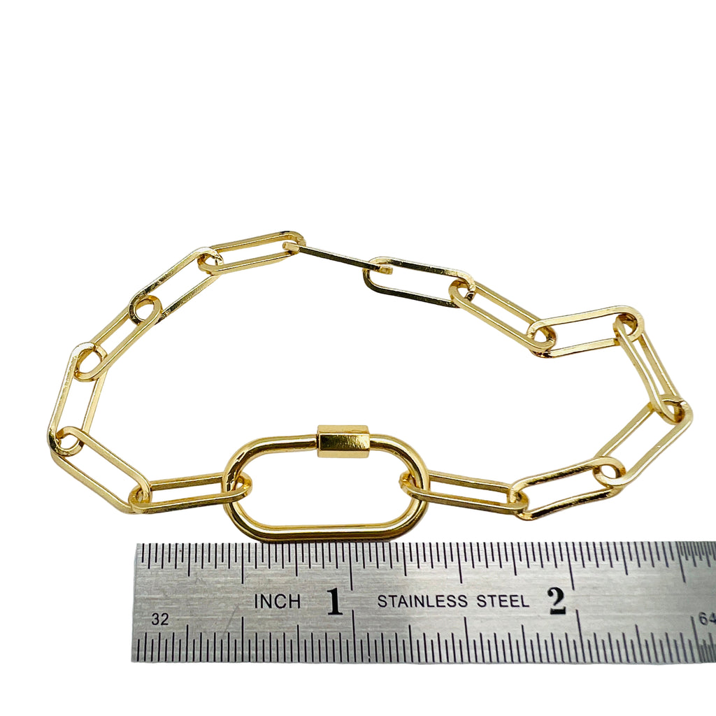 golden paperclip chain bracelet with carabiner clasp displayed over ruler with white background. 