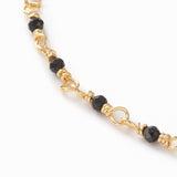 zoomed in section of golden chain and black spinel faceted round beaded necklace over white background. 