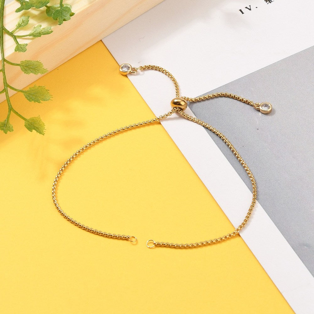 golden Bolo style bracelet making with slider bead and bezel set clear stone stopper beads on a yellow, white and gray background with green leaves.. 