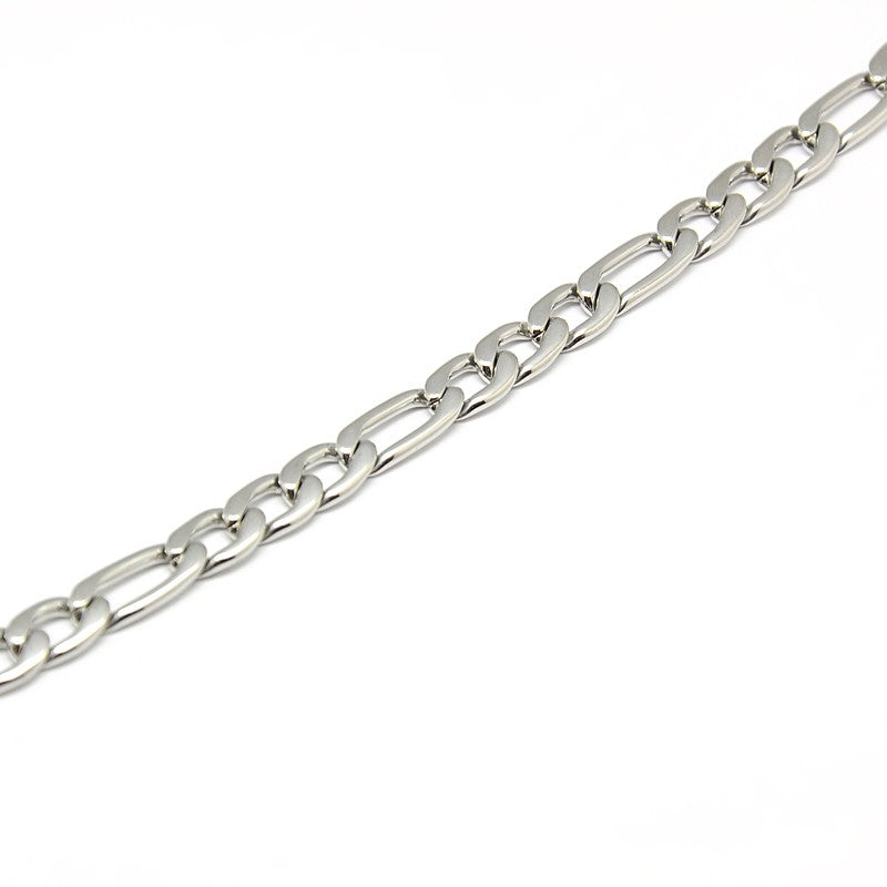 zoomed in section of silver tone Figaro chain necklace a white background. 