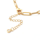 zoomed in section of lobster claw clasp and extender chain with bezel set clear stone on end of golden paperclip chain bracelet on a white background.