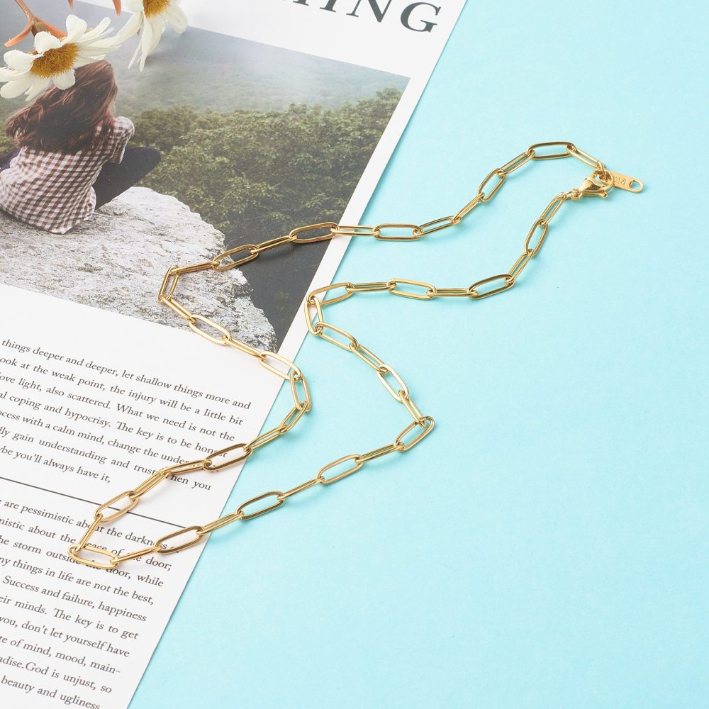 golden medium link paperclip chain necklace with lobster claw clasp on magazine article and light blue background.. 