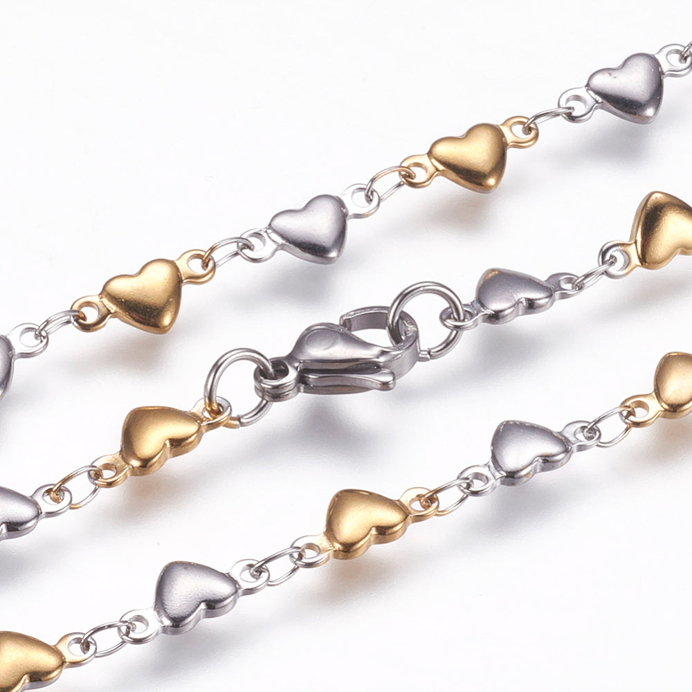 zoomed in sections of two-tone alternating stainless steel and golden flat heart link necklace with lobster claw clasp on white background. 
