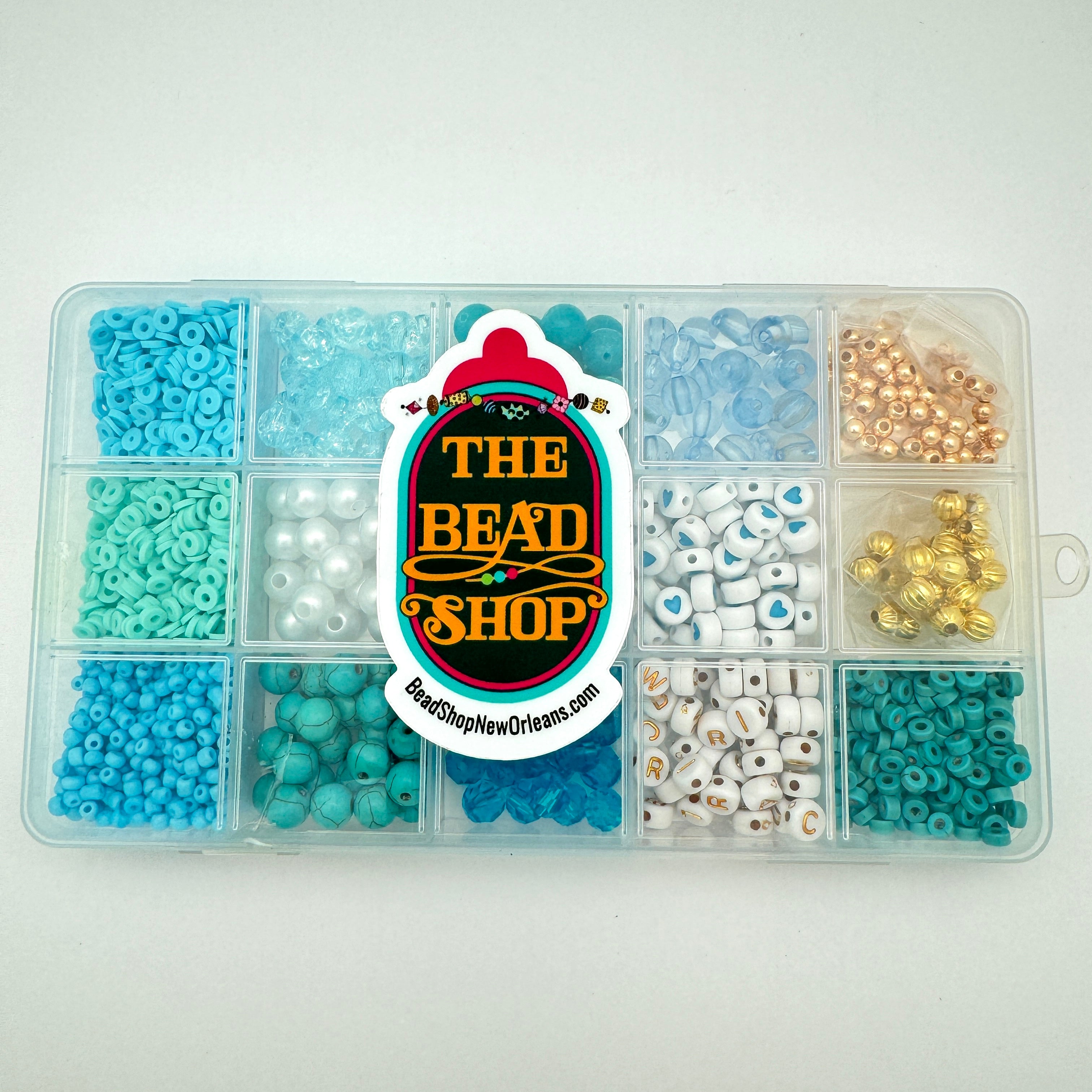 closed fifteen compartment plastic blue bead box with variety of blue and gold beads with The Bead Shop logo on front over white background. 