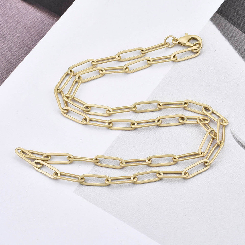 matte golden large paperclip link necklace with lobster claw clasp on white and gray photo background. 