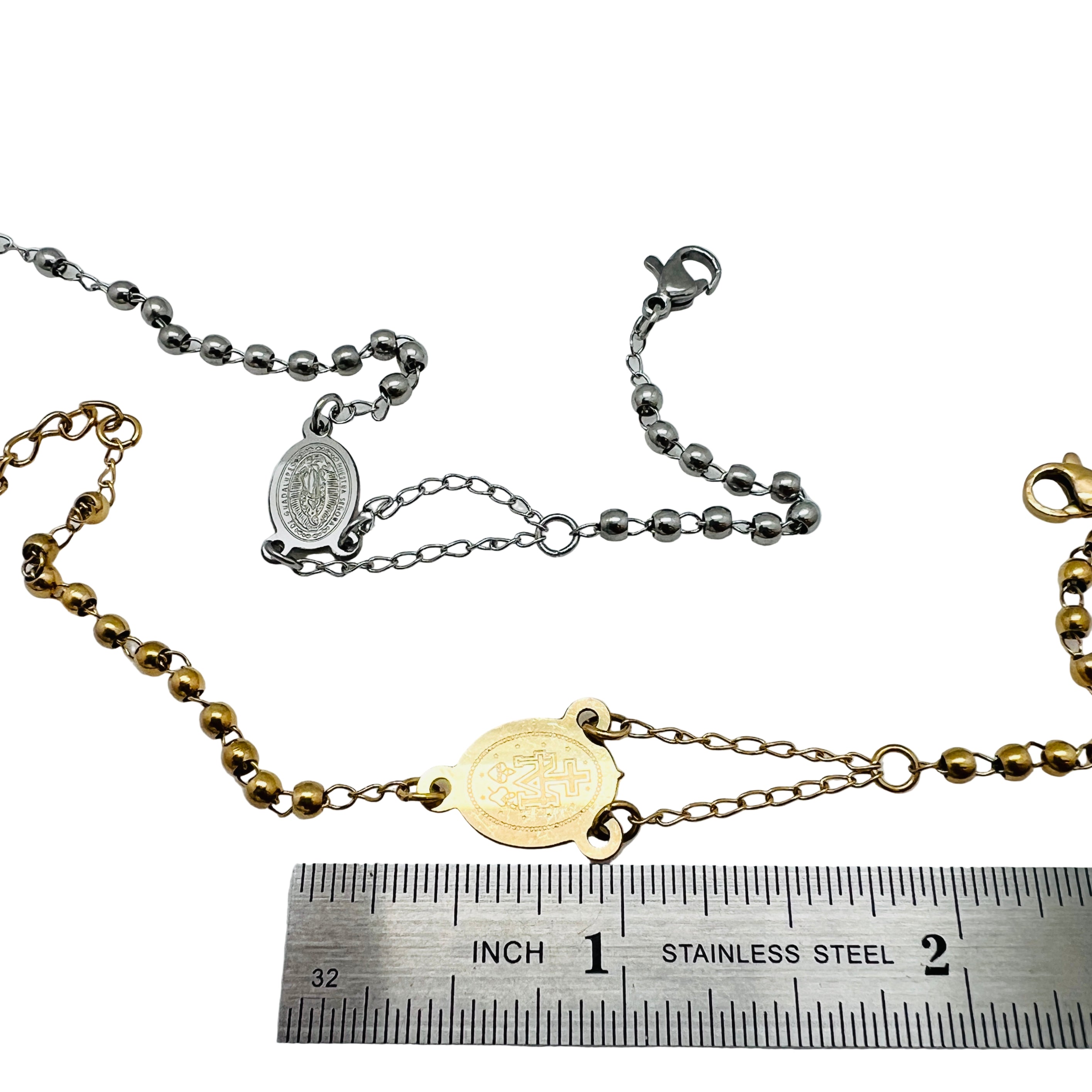 golden and silver tone rosary bracelets with Virgin Mary connector piece a ball link chain with lobster claw claps  displayed above a ruler with white background. 