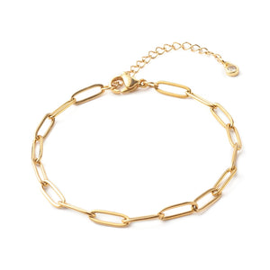 golden paperclip chain bracelet with lobster claw clasp and extender chain with bezel set clear stone on end shown on a white background.