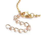 zoomed in portion of golden ball chain necklace with a lobster claw clasp and extender on a white background. 