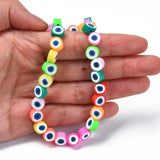 multicolor polymer clay round eye bead strand draped over hand with white background. 