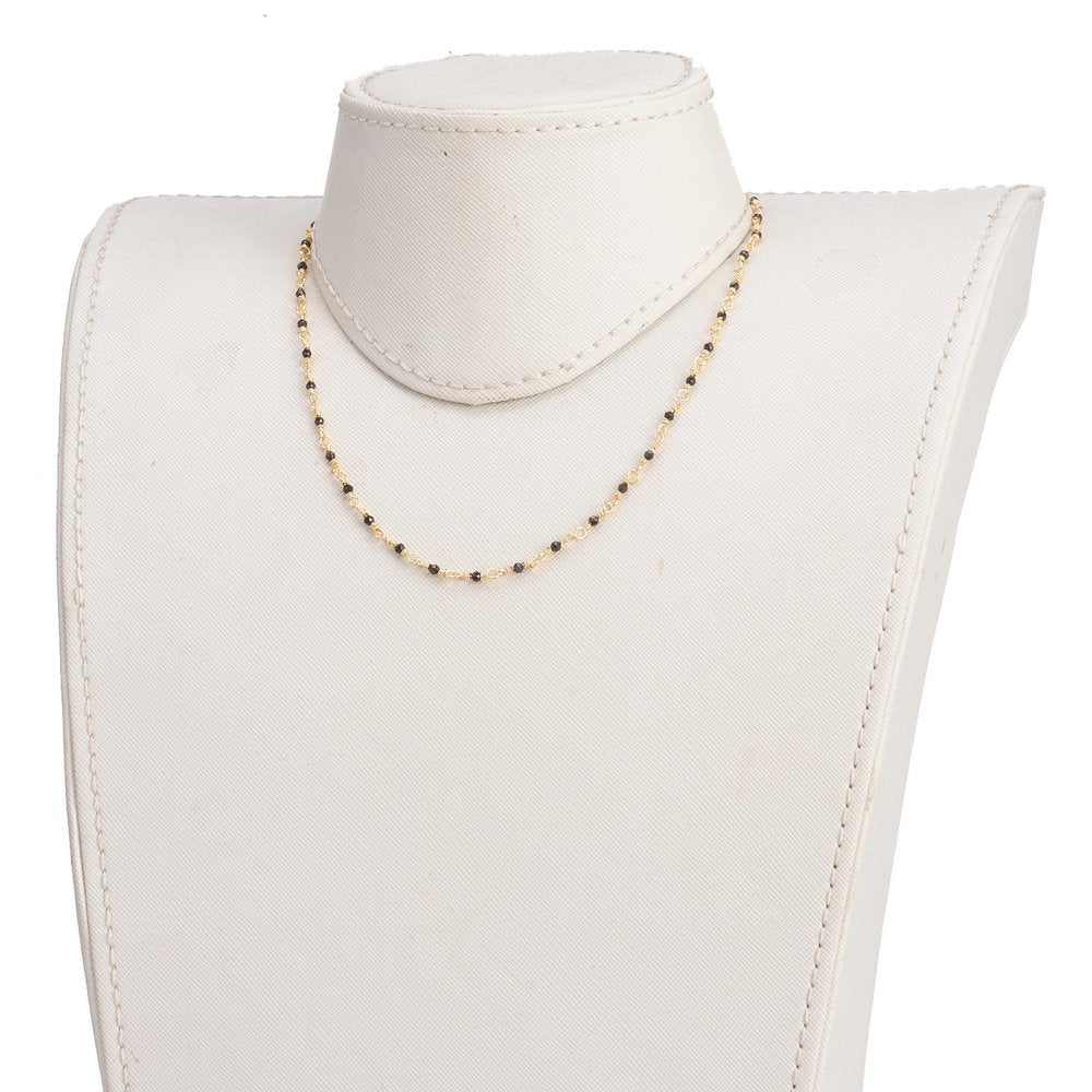 golden chain and black spinel faceted round beaded necklace on off-white neck form with white background. 