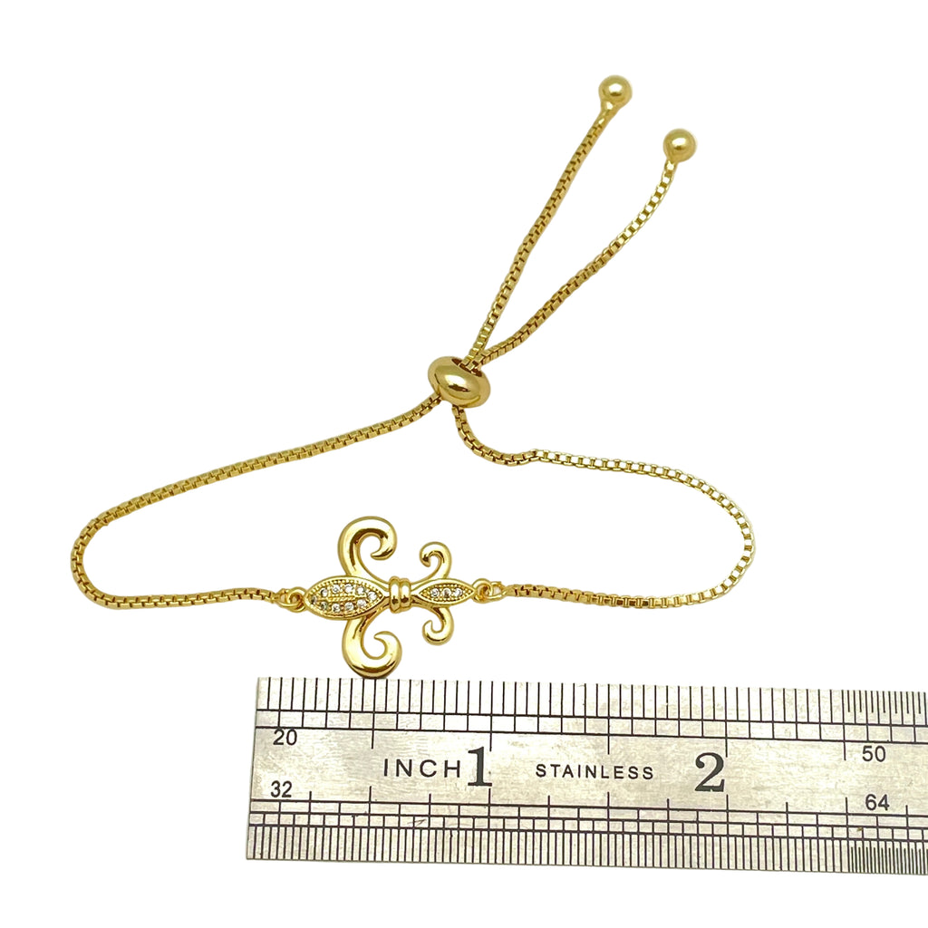 golden, micro pave set clear stone fleur de lis connector and box link bracelet with bolo style adjustable clasp on displayed above a stainless steel ruler on white background. 