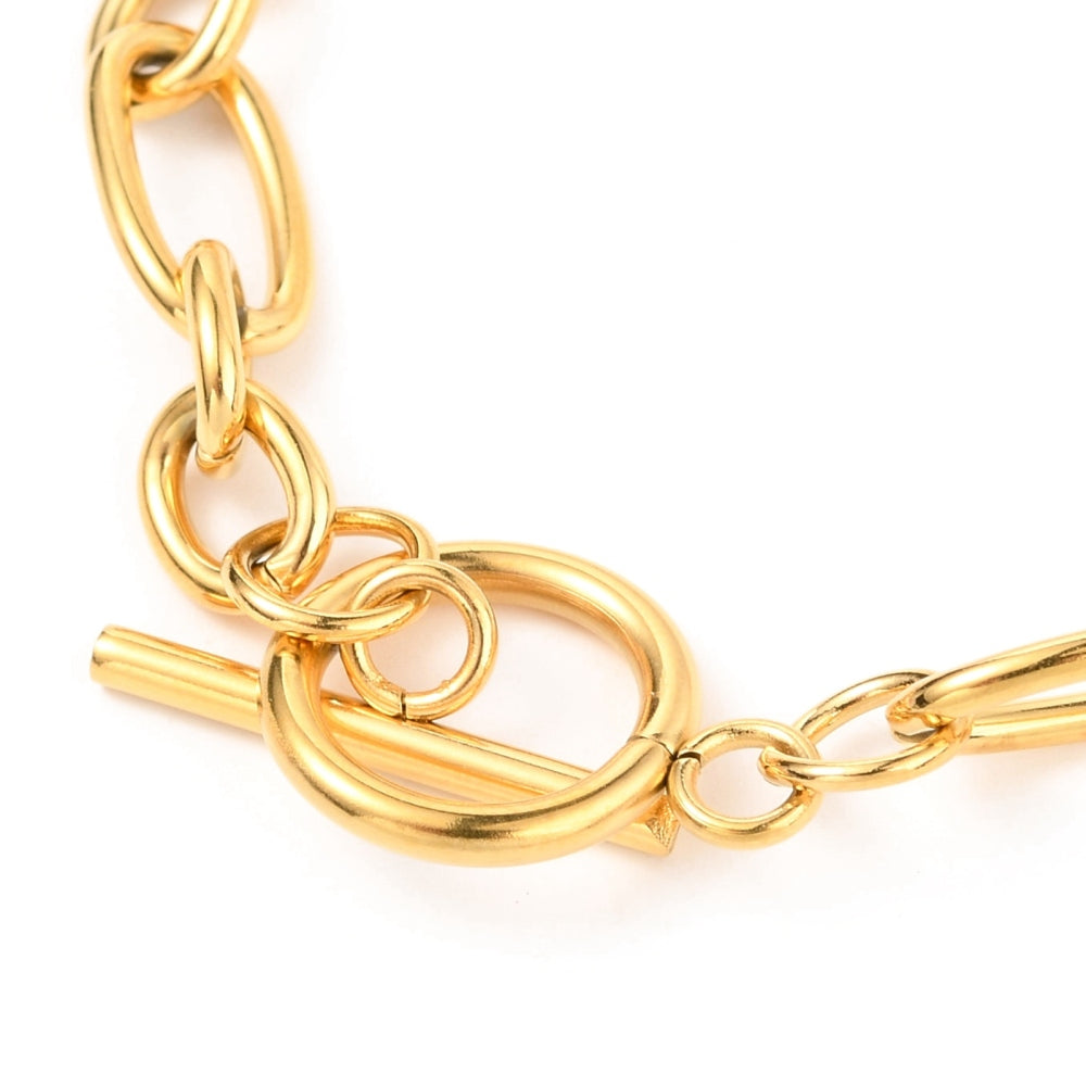 zoomed in golden toggle clasp on Figaro chain bracelet against a white background. 
