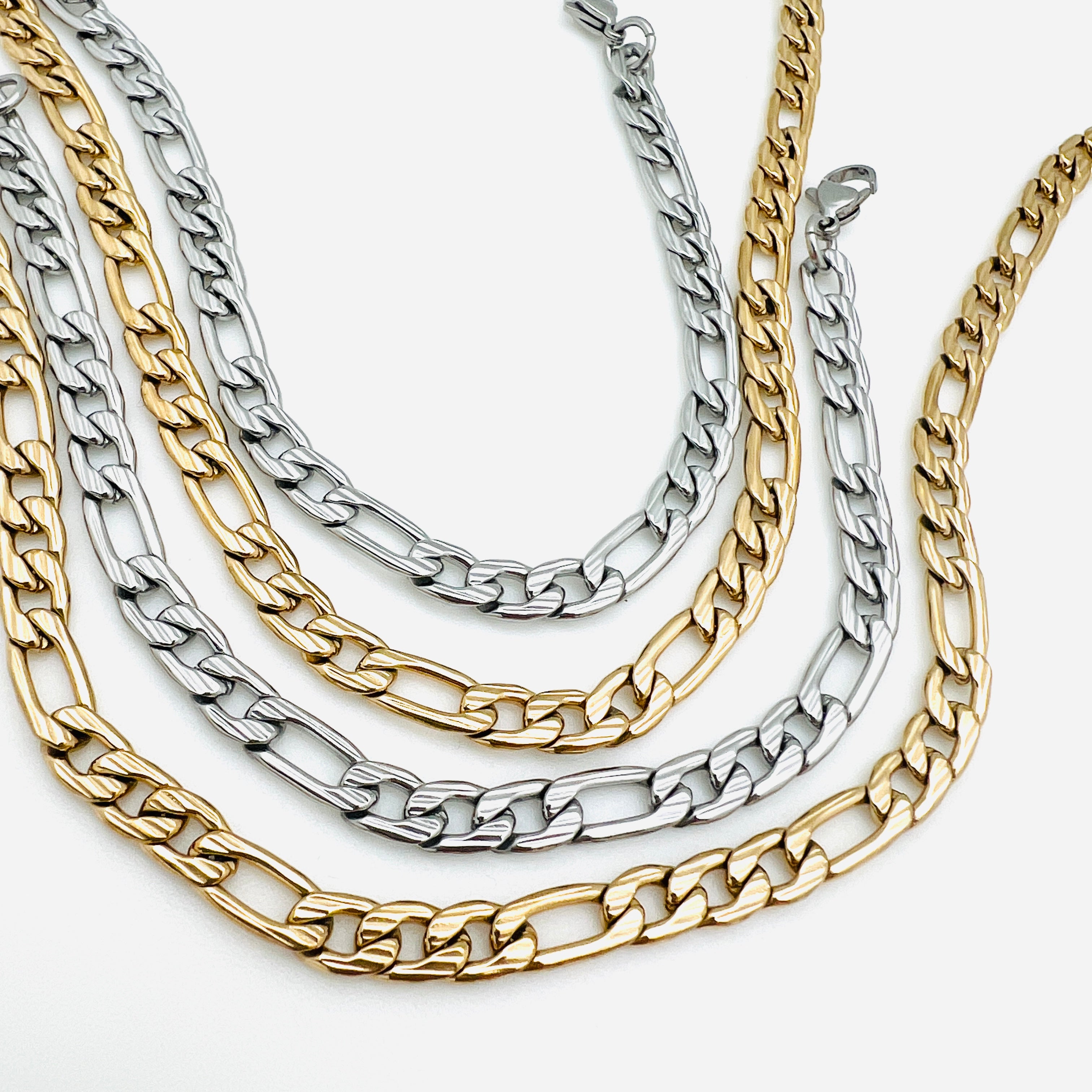 two silver tone and two golden textured Figaro link chains with lobster claw clasp on a white background.