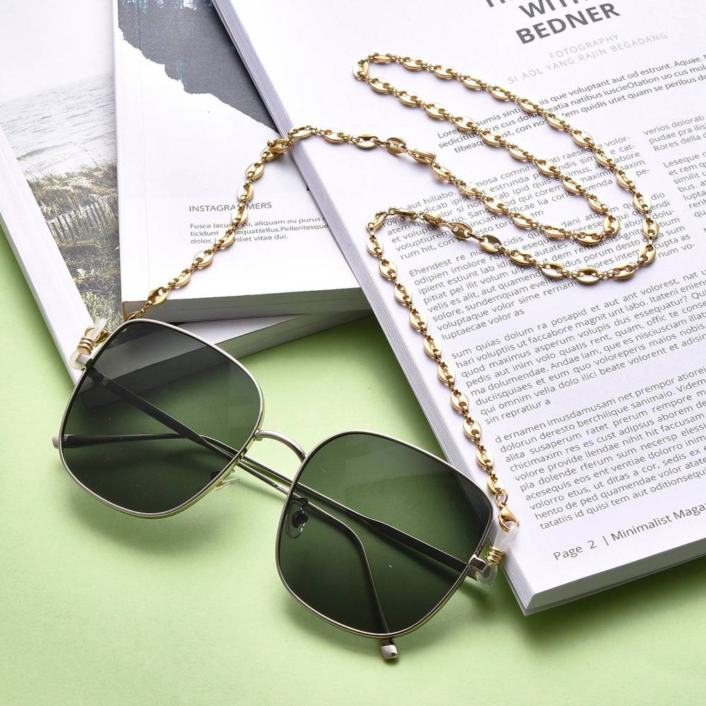 golden coffee bean link eyeglass chain with lobster claw clasps and rubber loop ends on sunglasses draped over some reading material on a green surface.