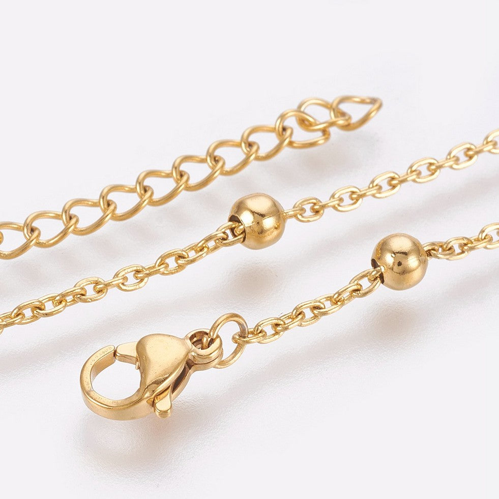 zoomed in sections of golden satellite chain anklet with lobster claw clasp and extender chain over white background. 