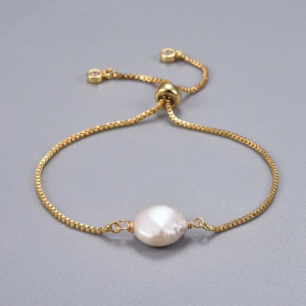 adjustable golden box chain bracelet featuring coin pearl with slider bead and bezel set charms on light grey surface. 