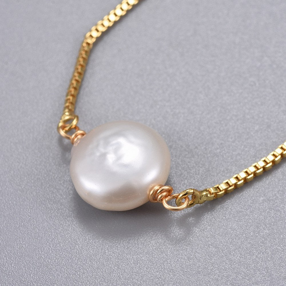 close-up of golden box chain bracelet featuring coin pearl on light grey surface. 