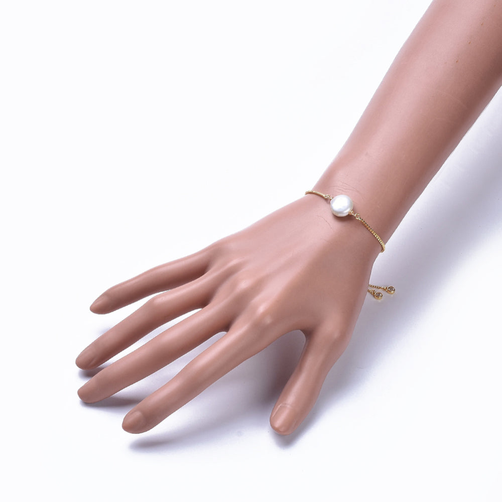 adjustable golden box chain bracelet featuring coin pearl and bezel set charms displayed on mannequin wrist over white background. 