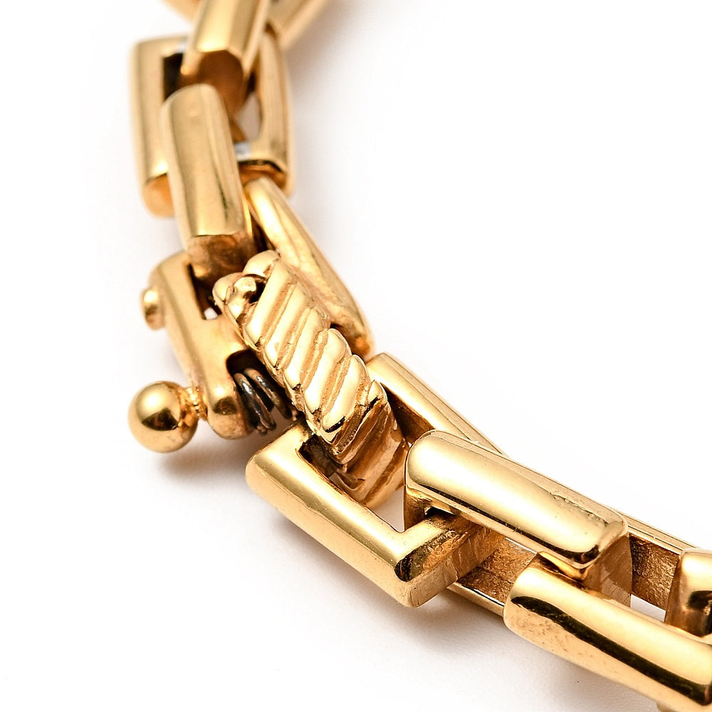 zoomed in golden hinged bracelet clasp on heavy rectangle link chain over white background. 