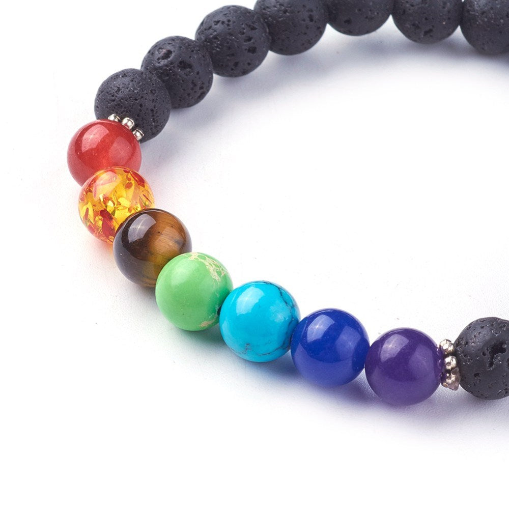 zoomed in section of black lava rock stretch chakra bracelet featuring seven round chakra stone beads between dotted silver spacer beads over a white background. 