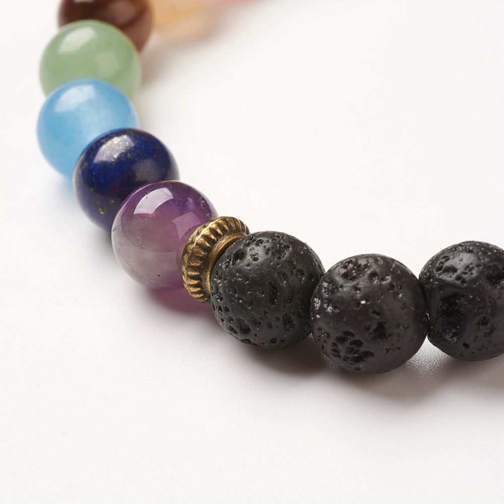 zoomed in section of black lava chakra bead bracelet featuring seven round chakra stone beads between antique spacer beads over white background. 