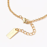 zoomed in section of golden rolo chain bracelet with lobster claw clasp and extender chain over white background. 