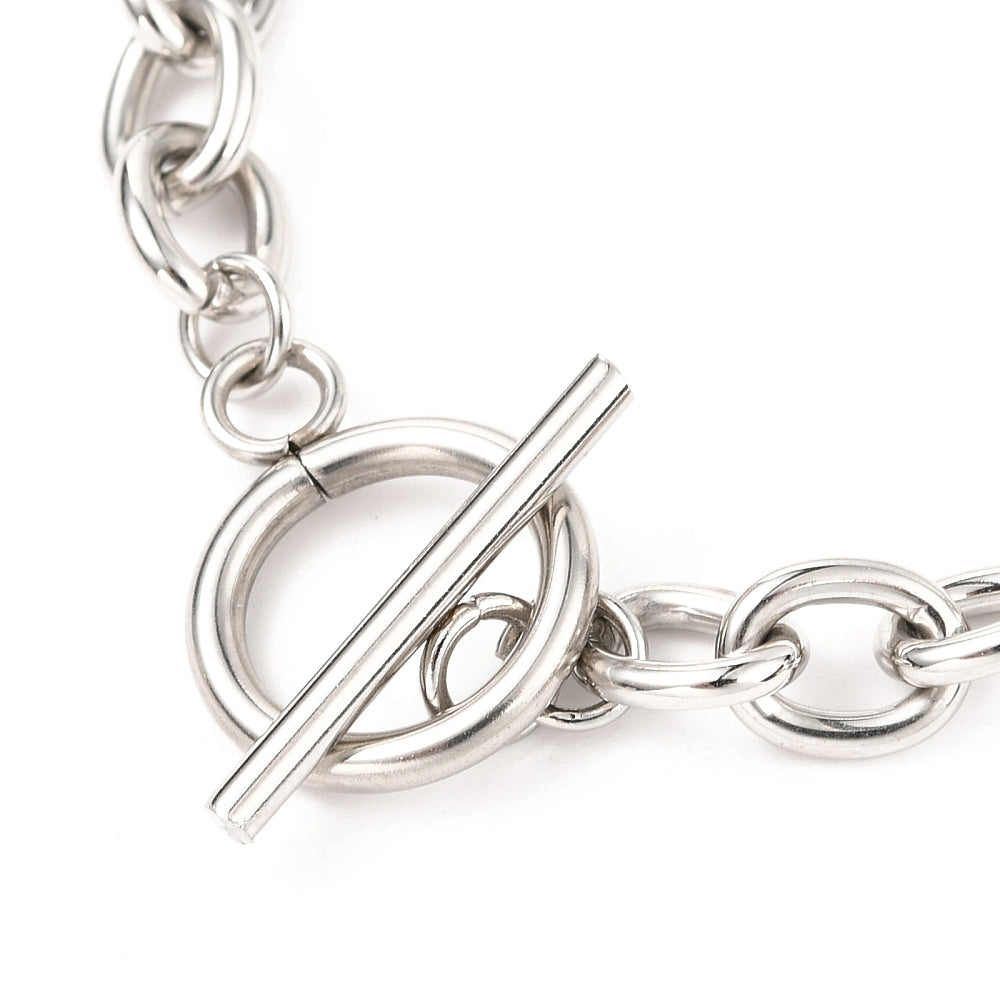 zoomed in silver toggle clasp on a Figaro chain bracelet against a white background. 