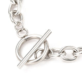 zoomed in silver toggle clasp on a Figaro chain bracelet against a white background. 