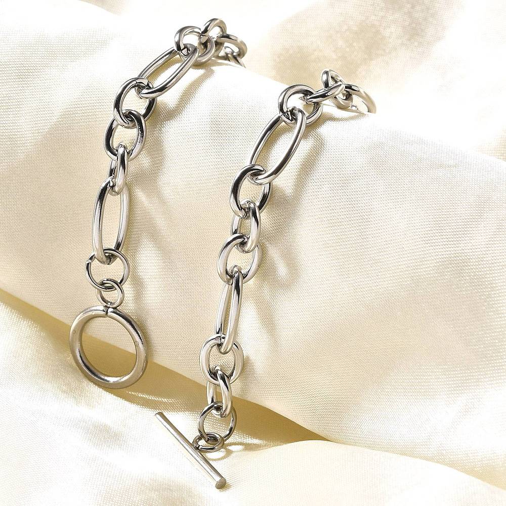 silver Figaro chain bracelet with toggle clasp draped over cream colored fabric.