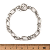silver Figaro chain bracelet with toggle clasp displayed above a wooden imperial ruler on white background. 