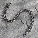 silver tone rolo chain bracelet over grey rock surface. 