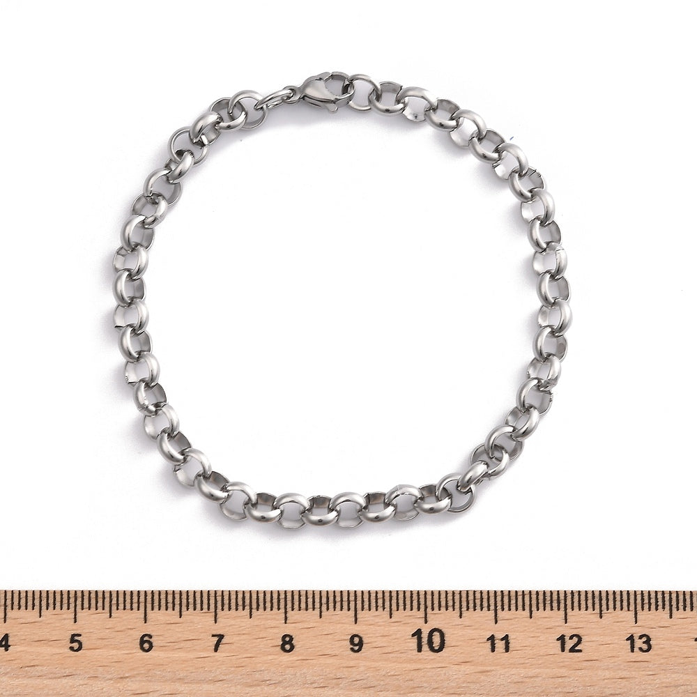 silver tone rolo chain bracelet with lobster claw clasp displayed above wooden ruler with white background .