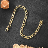 golden Figaro link bracelet with lobster claw clasp on black textured background with orange stone in corner. 