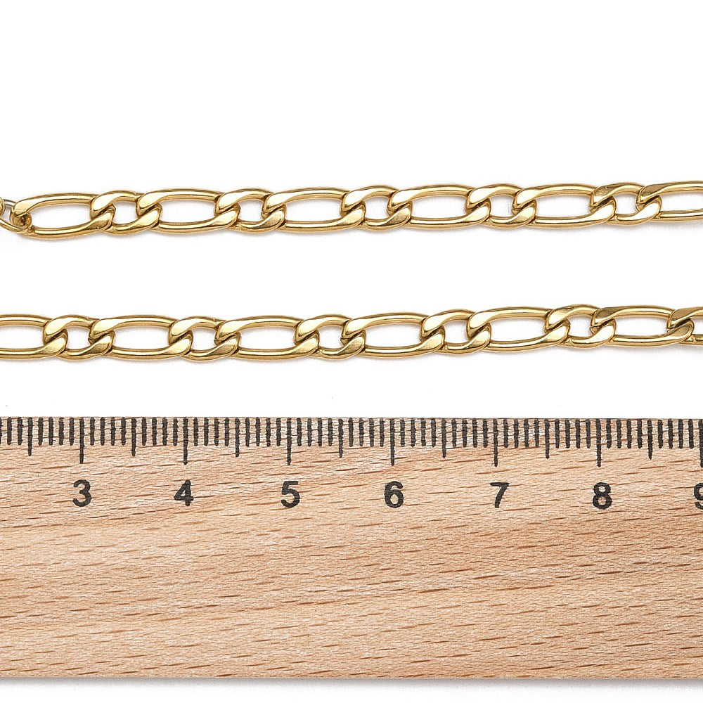 golden Figaro link bracelet with lobster claw clasp displayed above a wooden ruler on white background. 