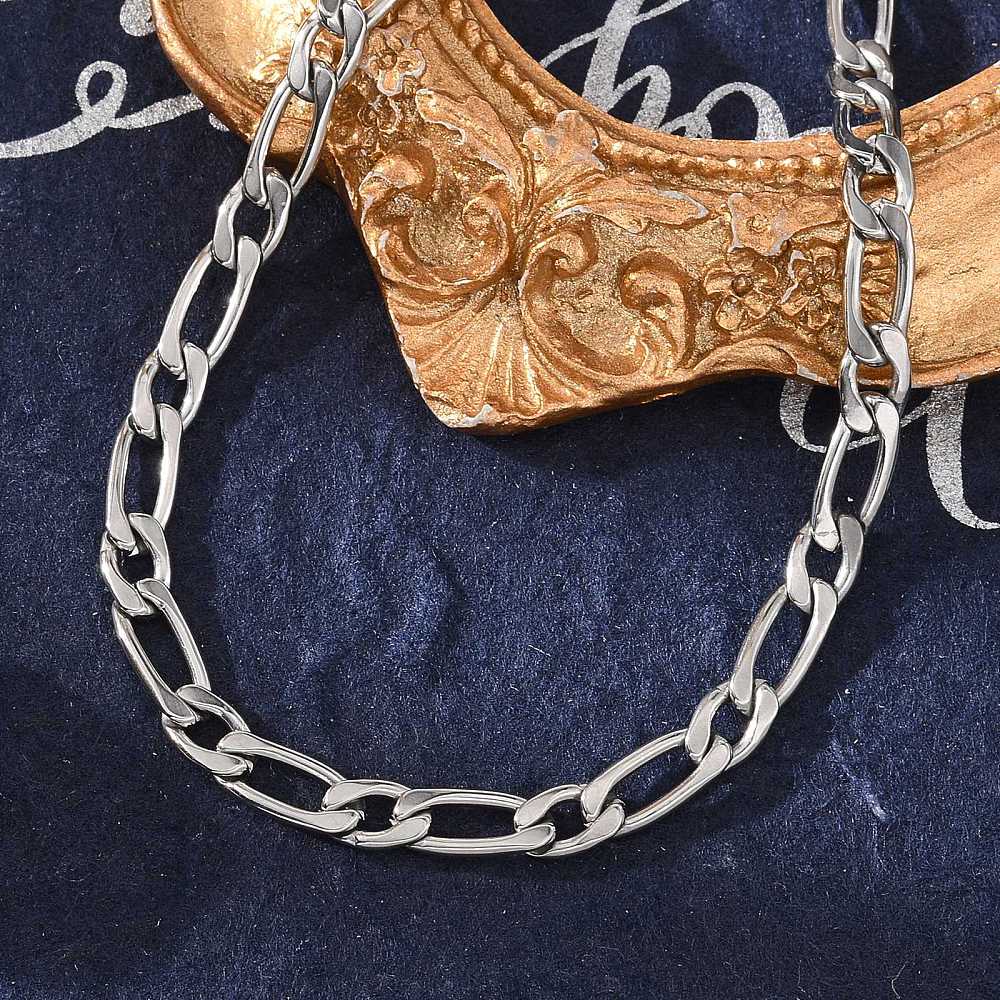 silver Figaro link bracelet displayed over an ornate golden picture frame above a blue felt background. 