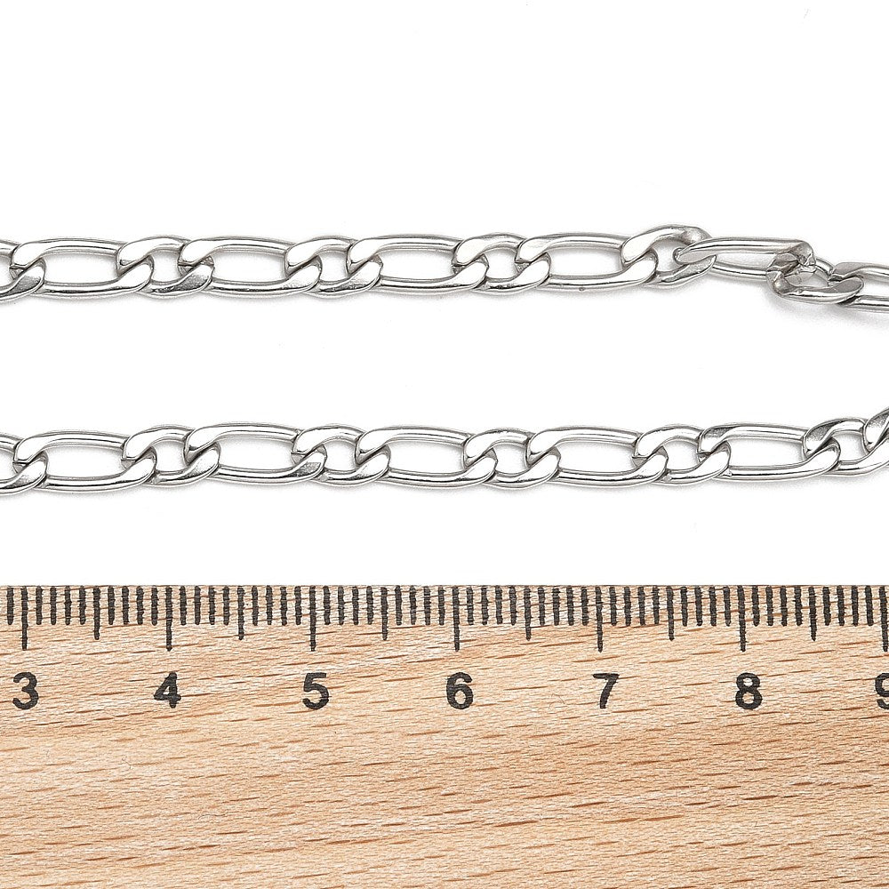 silver Figaro link bracelet with lobster claw clasp displayed above a wooden ruler on white background. 