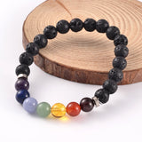 black lava rock stretch chakra bracelet featuring seven round chakra stone beads between smooth silver tone spacer beads over a white background. 