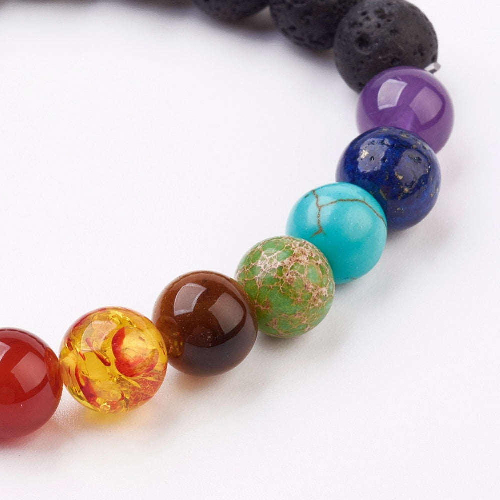 zoomed in section of black lava rock stretch chakra bracelet featuring seven round chakra stone beads on white background. 